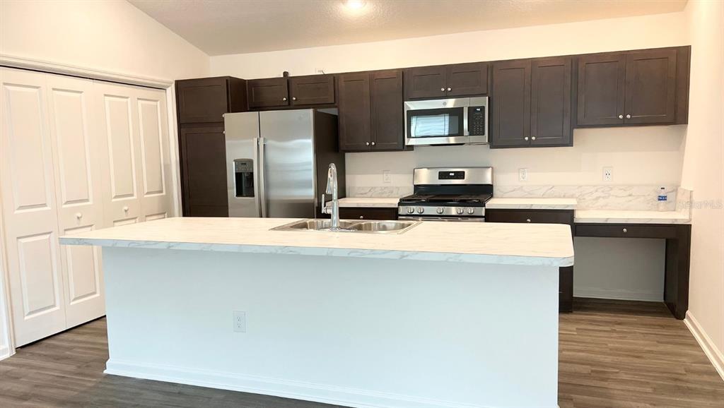 A kitchen features dark wood cabinets, stainless steel appliances, and a white marble-look island countertop — 6487 PETER LANE, THE VILLAGES, FL