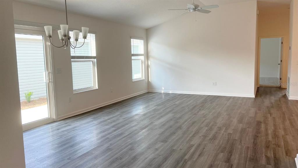 An empty living room features light-colored walls, wood-look flooring, a ceiling fan, and sliding doors — 6487 PETER LANE, THE VILLAGES, FL