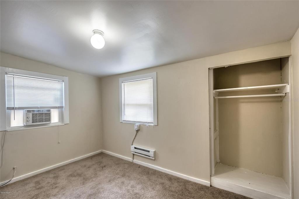 A bedroom with beige walls, carpeted flooring, two windows, and an open closet — 312 FRANCES TERRACE, DAYTONA BEACH, FL