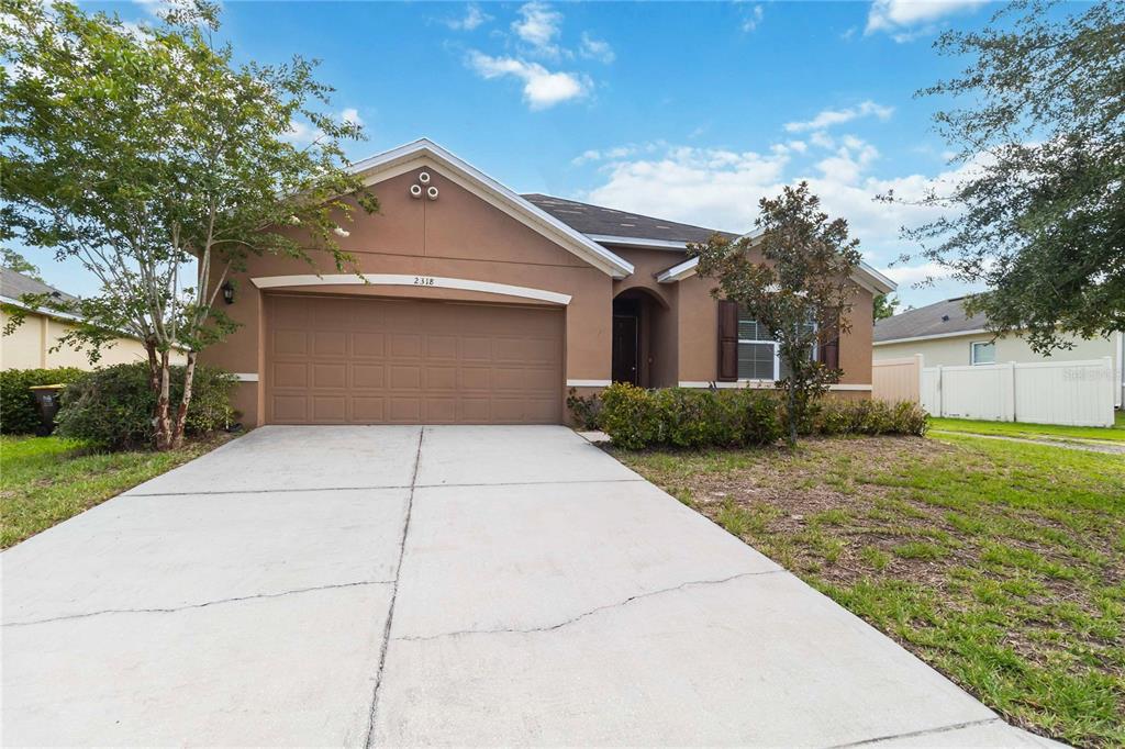 A tan, single-story suburban house with a two-car garage and a concrete driveway — 2318 SEQUOIA WAY, DAVENPORT, FL