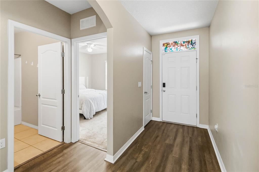 An entryway with wood-look flooring leads to a bedroom and a tiled bathroom — 2318 SEQUOIA WAY, DAVENPORT, FL