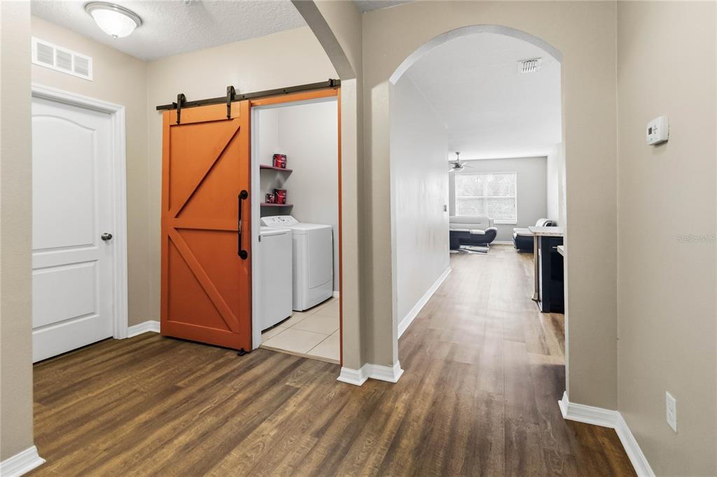 A hallway features wood-look flooring, an orange barn door to a laundry room, and arched entryways — 2318 SEQUOIA WAY, DAVENPORT, FL