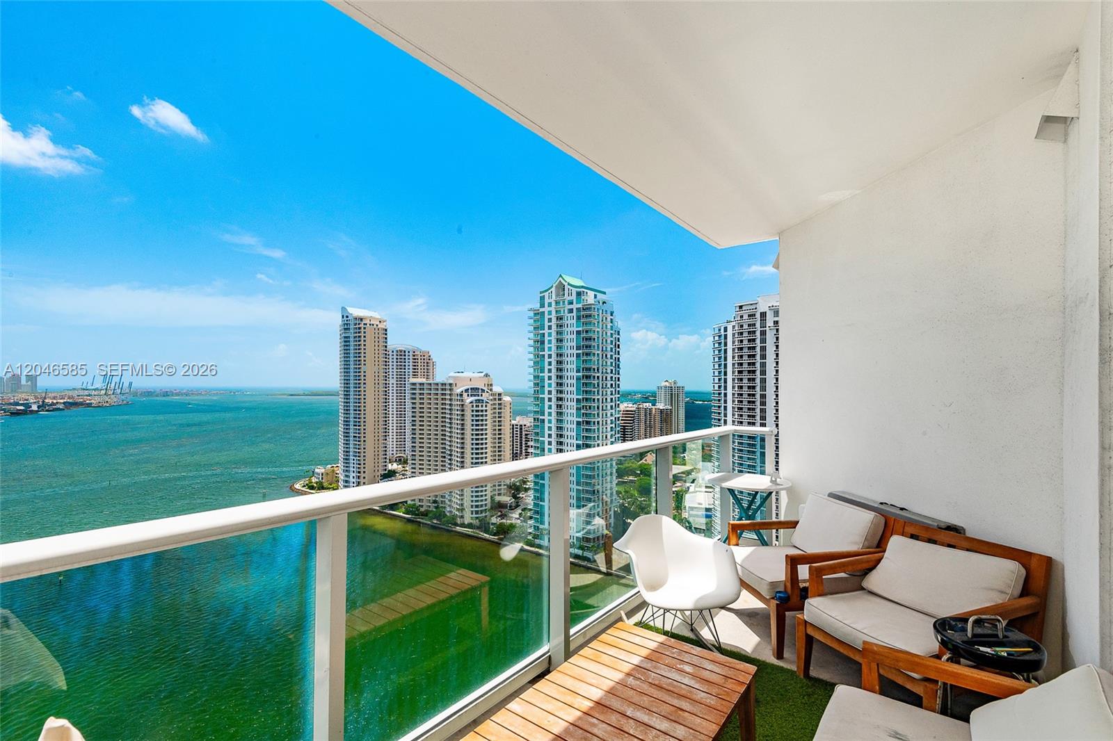 A balcony with outdoor furniture overlooks a bay and a city skyline — 300 S Biscayne Blvd # 2612, Miami FL 33131, MIAMI, FL