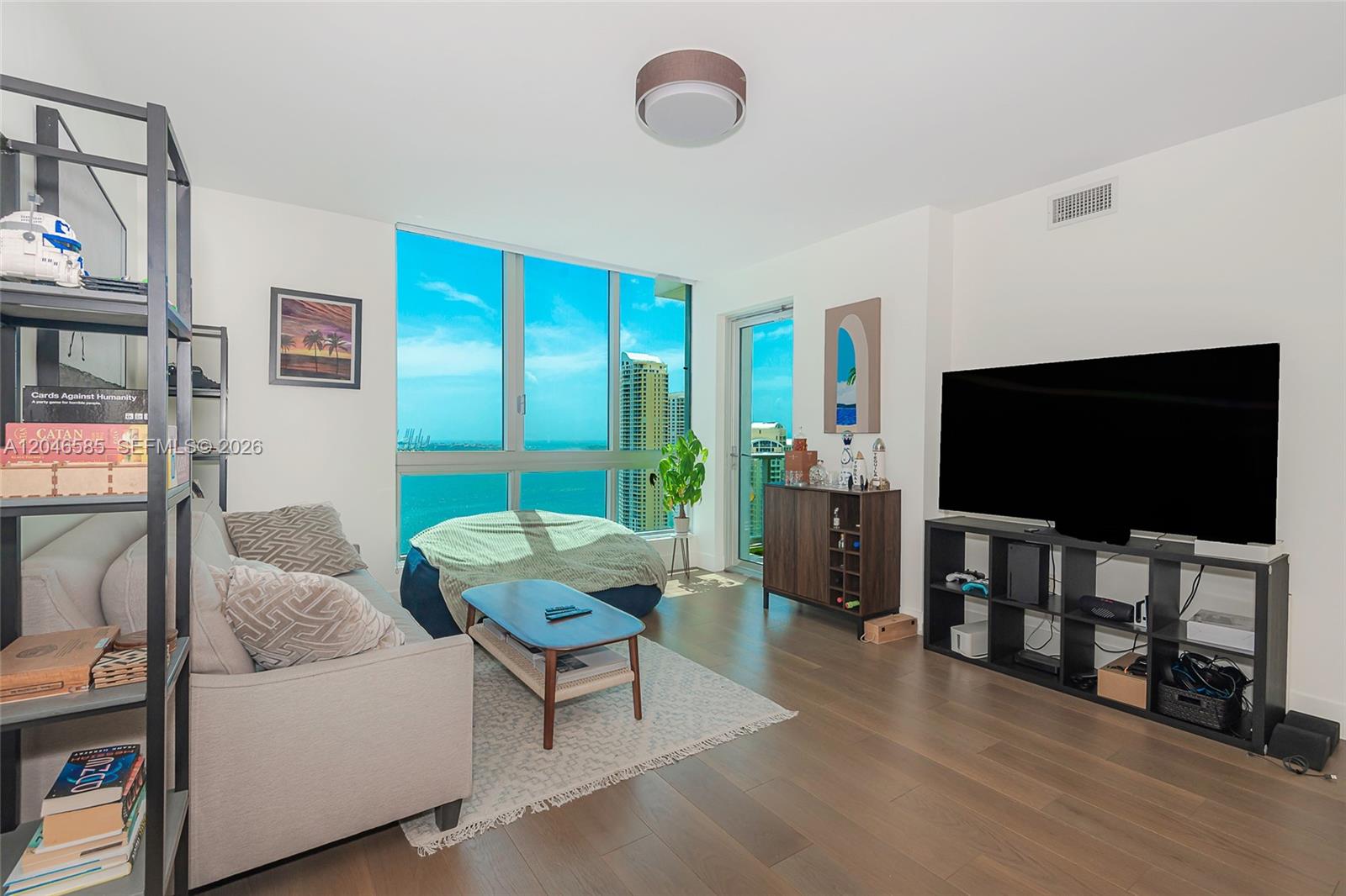 A living room features a sofa, a television on a shelf, and floor-to-ceiling ocean views — 300 S Biscayne Blvd # 2612, Miami FL 33131, MIAMI, FL