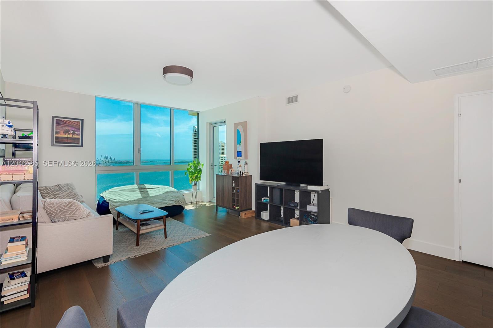A living and dining area features dark wood floors, a large window, and ocean views — 300 S Biscayne Blvd # 2612, Miami FL 33131, MIAMI, FL