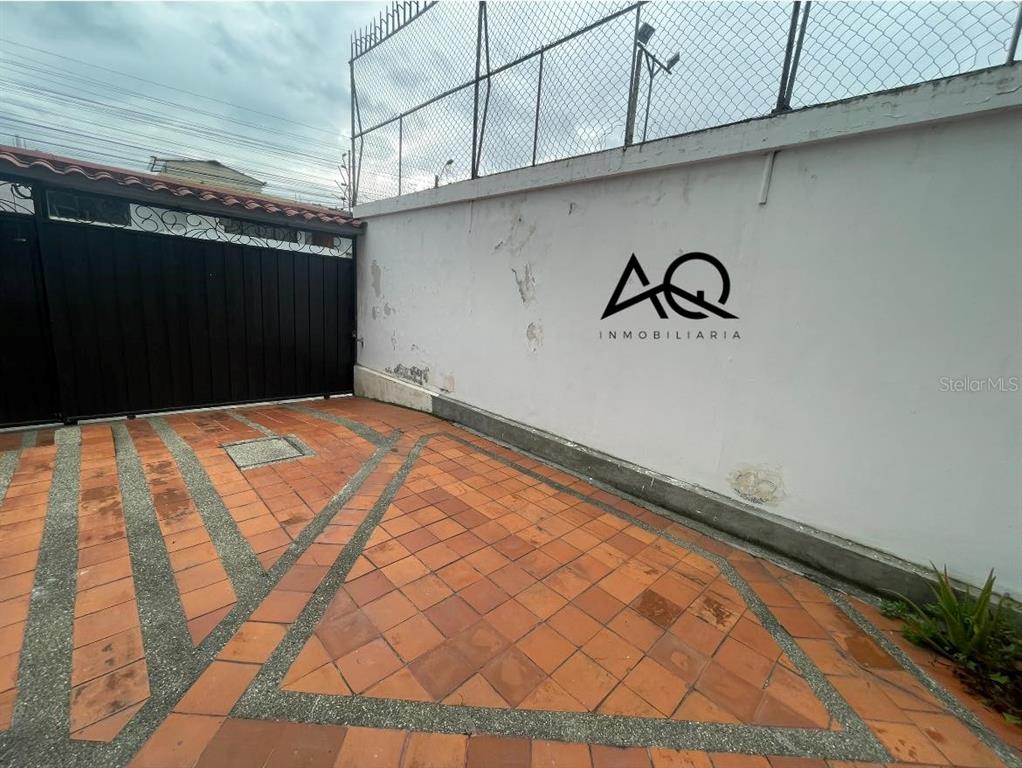 A paved driveway leads to a black metal gate and a white wall with signage — 2820 PEDRO VICENTE MALDONADO, LOJA/ECUADOR, OC