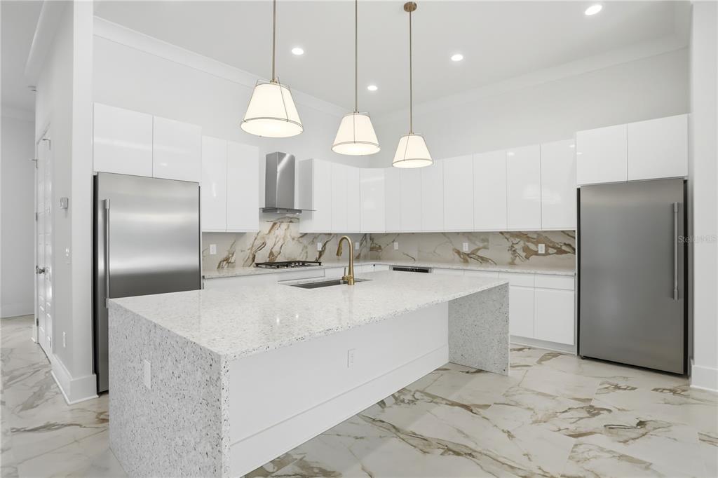 A modern kitchen features white cabinets, a speckled island, stainless steel appliances, and marble flooring — 7626 WHITEMARSH WAY, KISSIMMEE, FL