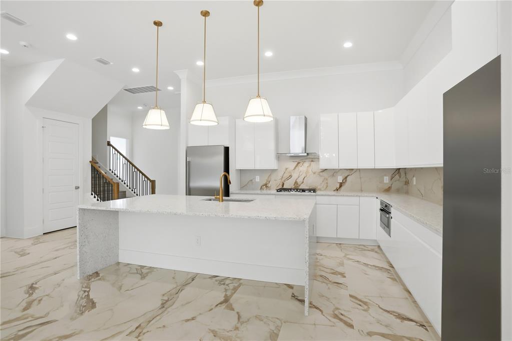 A modern white kitchen features a large island, marble-patterned flooring, and gold pendant lighting — 7626 WHITEMARSH WAY, KISSIMMEE, FL