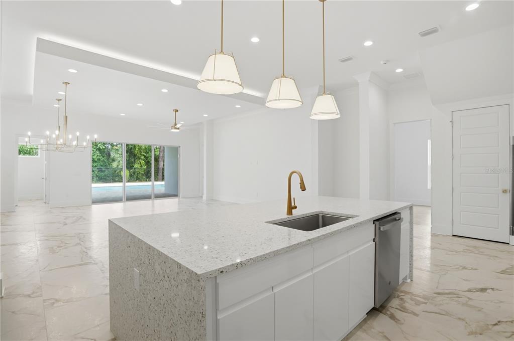 A modern kitchen island with a sink and white cabinets sits in a bright, open-concept room — 7626 WHITEMARSH WAY, KISSIMMEE, FL