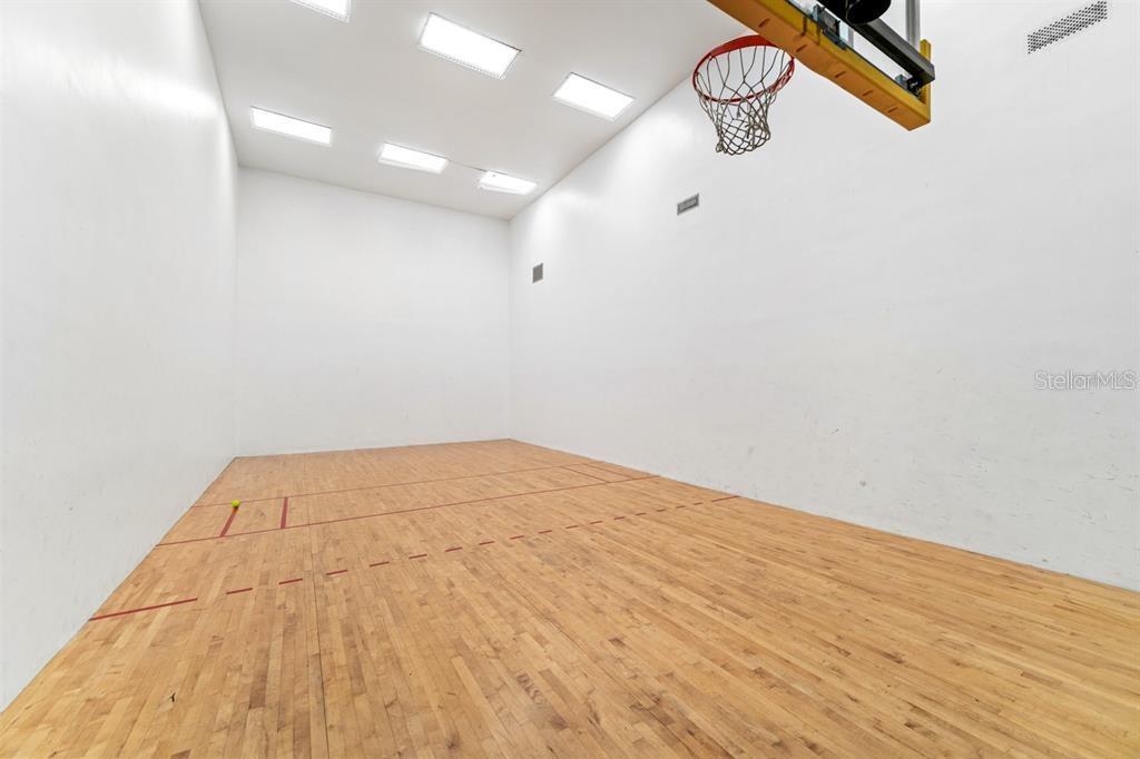 An indoor racquetball court features a hardwood floor, white walls, and a mounted basketball hoop — 4126 CENTRAL SARASOTA PARKWAY UNIT 2012, SARASOTA, FL
