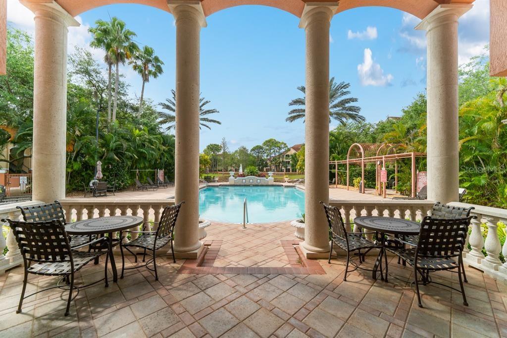 A covered patio with stone columns overlooks a swimming pool surrounded by palm trees — 4126 CENTRAL SARASOTA PARKWAY UNIT 2012, SARASOTA, FL