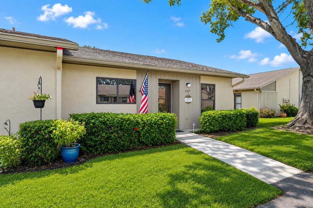 A single-story house with a beige exterior, a green hedge, and an American flag — 2707 60TH AVENUE TERRACE W, BRADENTON, FL