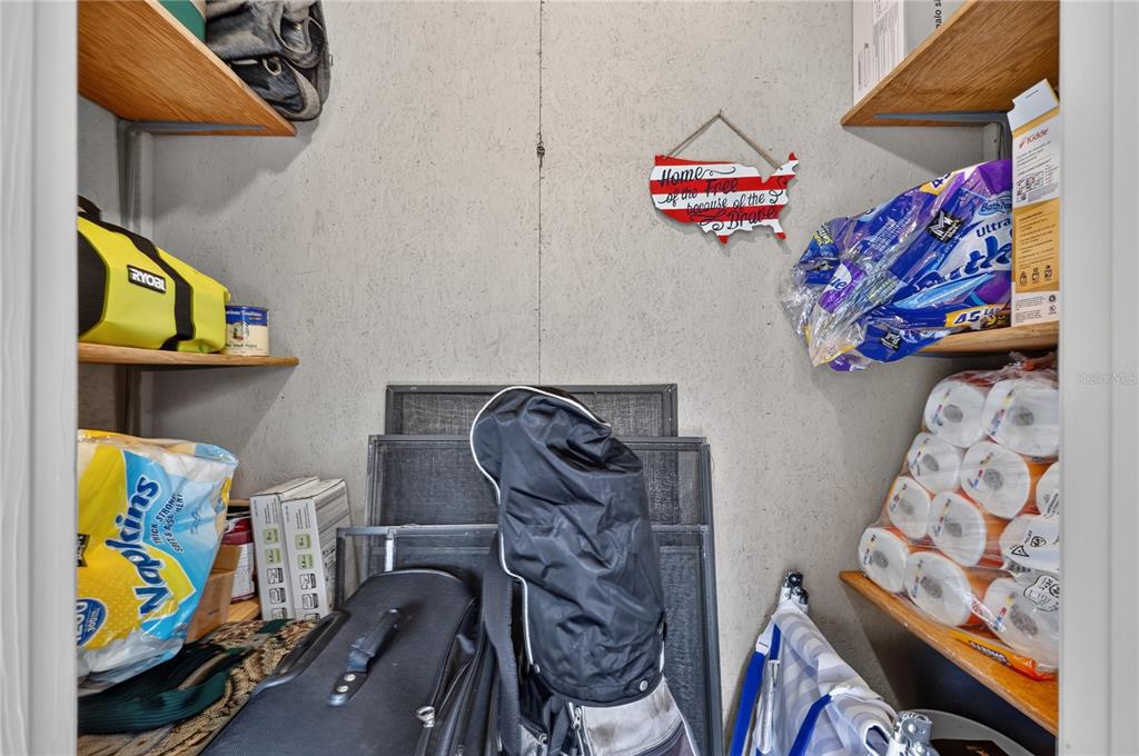 A small storage closet with wooden shelves holding household supplies, luggage, and miscellaneous items — 2707 60TH AVENUE TERRACE W, BRADENTON, FL