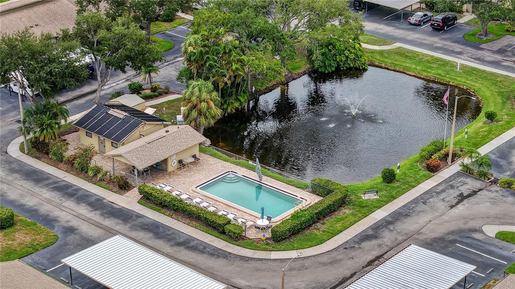 An aerial view shows a community swimming pool, clubhouse, and pond surrounded by parking areas — 2707 60TH AVENUE TERRACE W, BRADENTON, FL