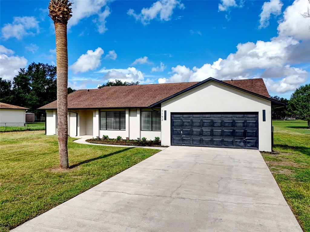 A single-story house with a white exterior, dark garage door, and a palm tree in front — 1192 LIZA STREET, ST CLOUD, FL
