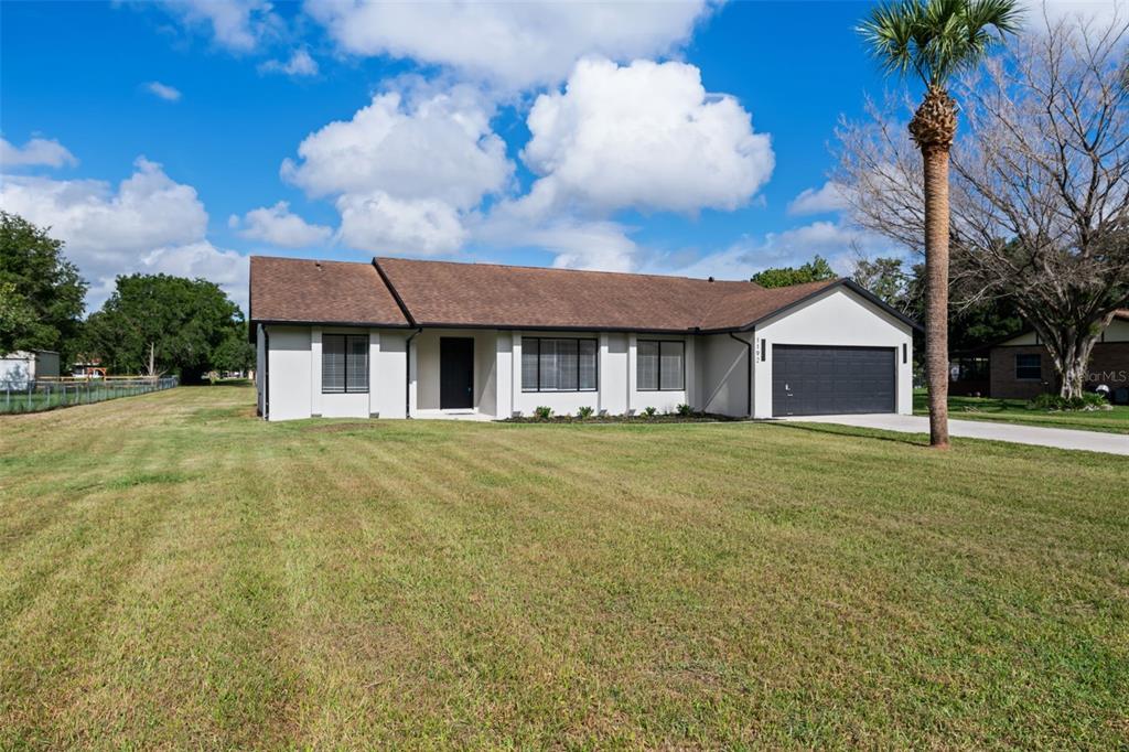 A single-story house with a white exterior, brown roof, and attached garage sits on a lawn — 1192 LIZA STREET, ST CLOUD, FL