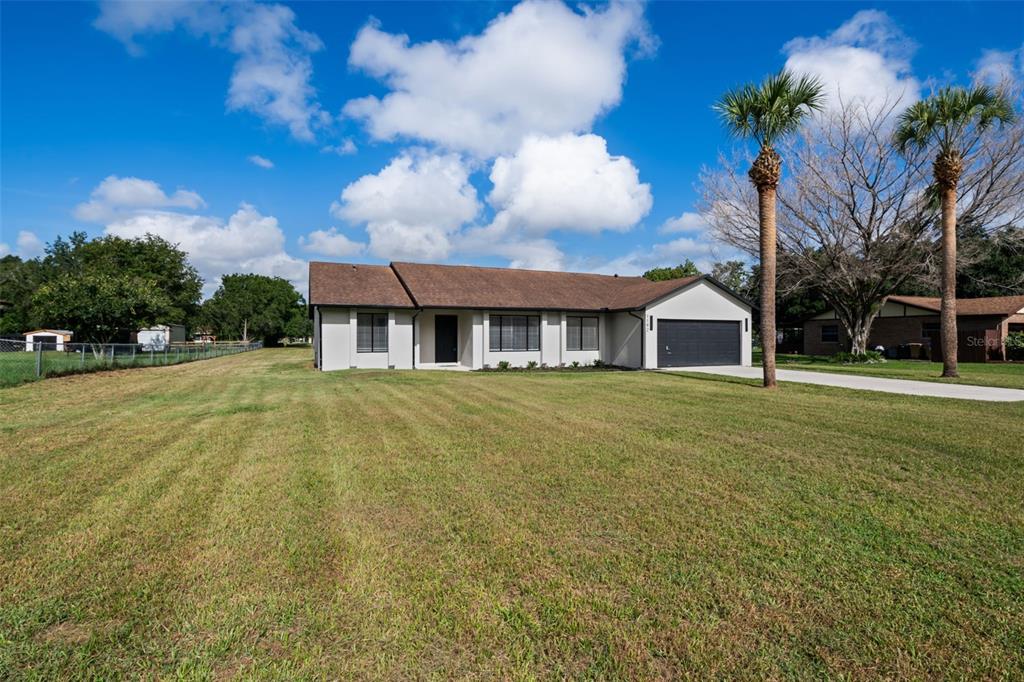 A single-story house with a brown roof, white exterior, and attached garage sits on a lawn — 1192 LIZA STREET, ST CLOUD, FL