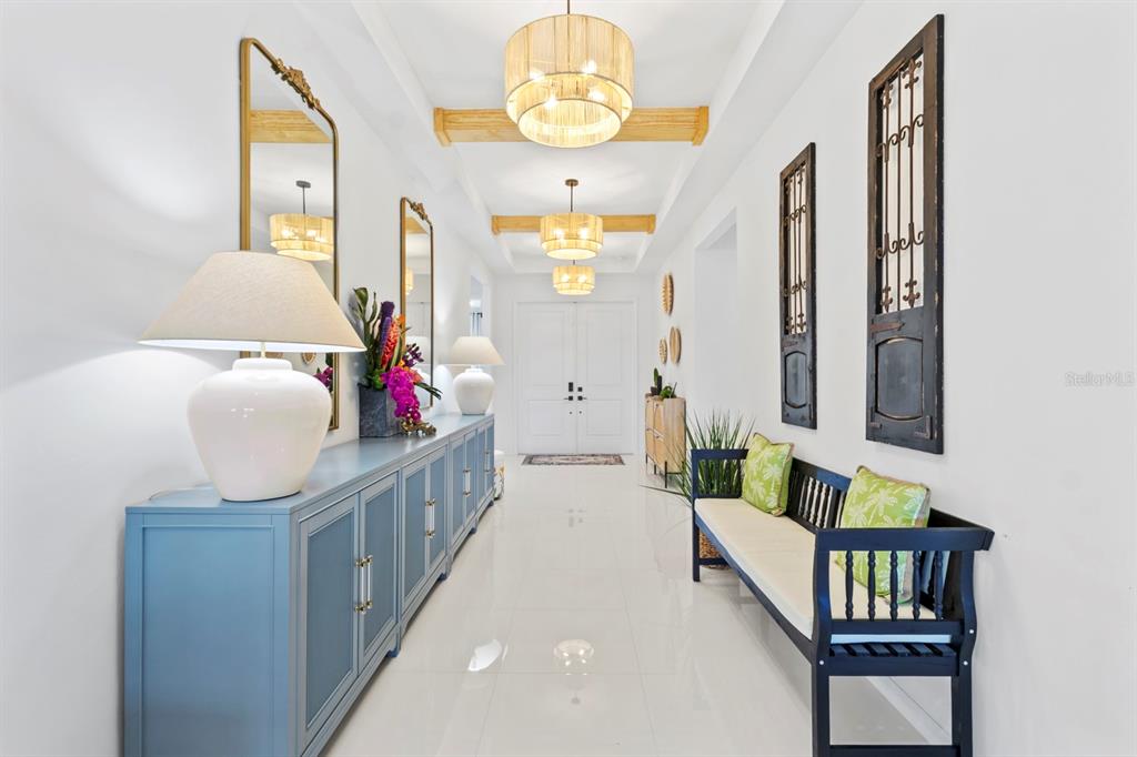 A bright, tiled hallway features blue cabinets, a wooden bench, and three hanging drum chandeliers — 16261 PRESERVATION BOULEVARD, PUNTA GORDA, FL