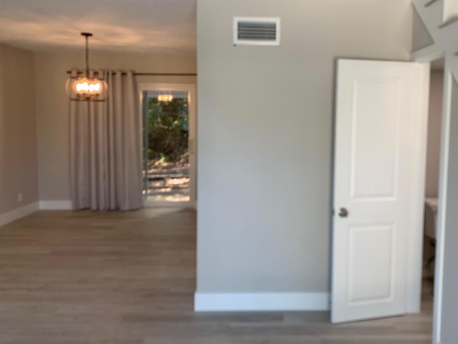 A room with light wood flooring, a chandelier, a sliding glass door, and a door — 4220 NE Indian River Dr. Drive # 2, Jensen Beach FL 34957, JENSEN BEACH, FL