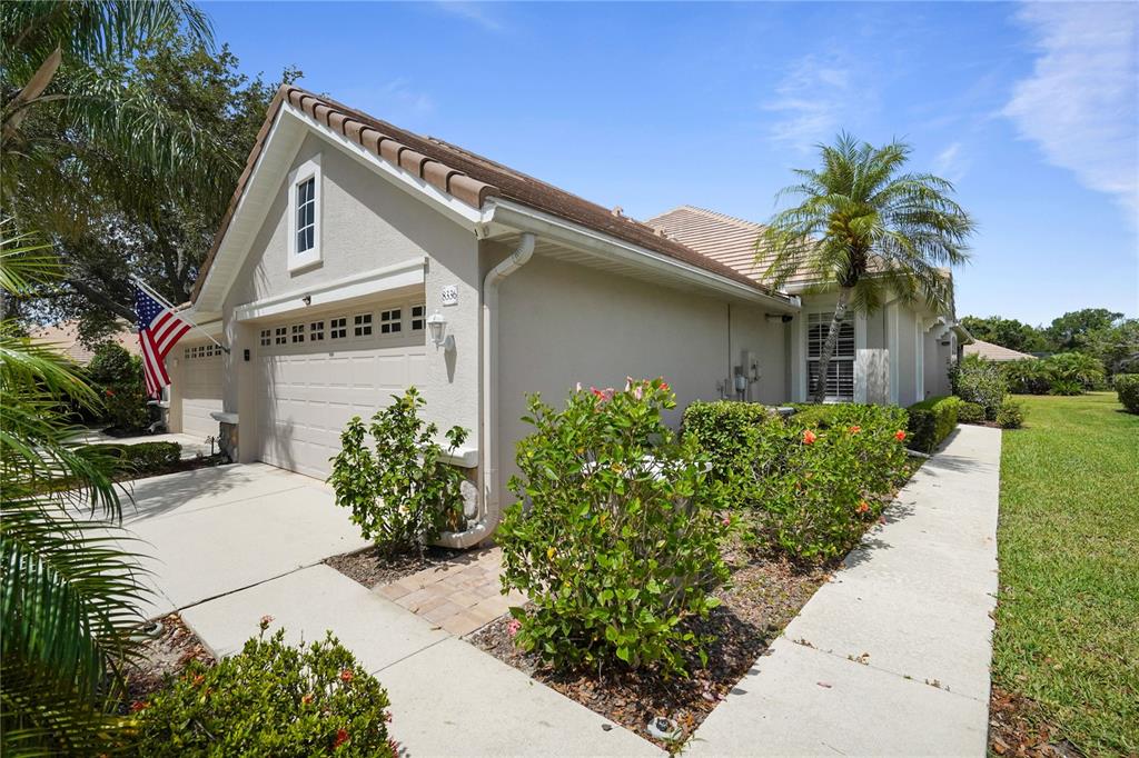 A beige house exterior features a two-car garage, a palm tree, and landscaped shrubbery — 8336 TARTAN FIELDS CIRCLE, LAKEWOOD RANCH, FL