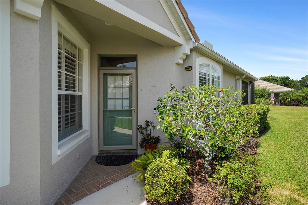 The exterior of a house features a front door with a storm door and landscaping — 8336 TARTAN FIELDS CIRCLE, LAKEWOOD RANCH, FL