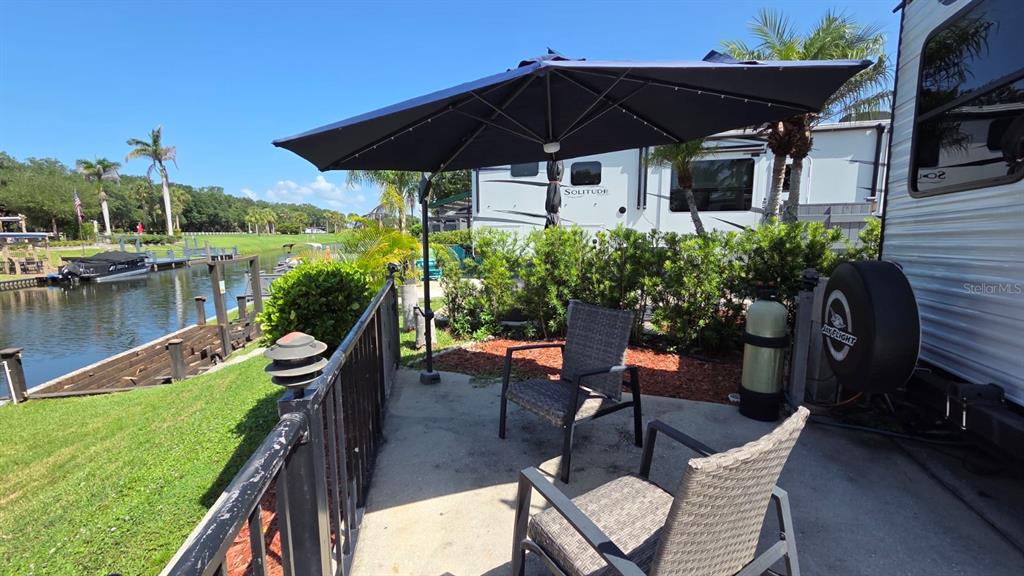 A patio with two chairs and an umbrella sits beside a parked recreational vehicle — 579 WATERWAY DRIVE, RIVER RANCH, FL