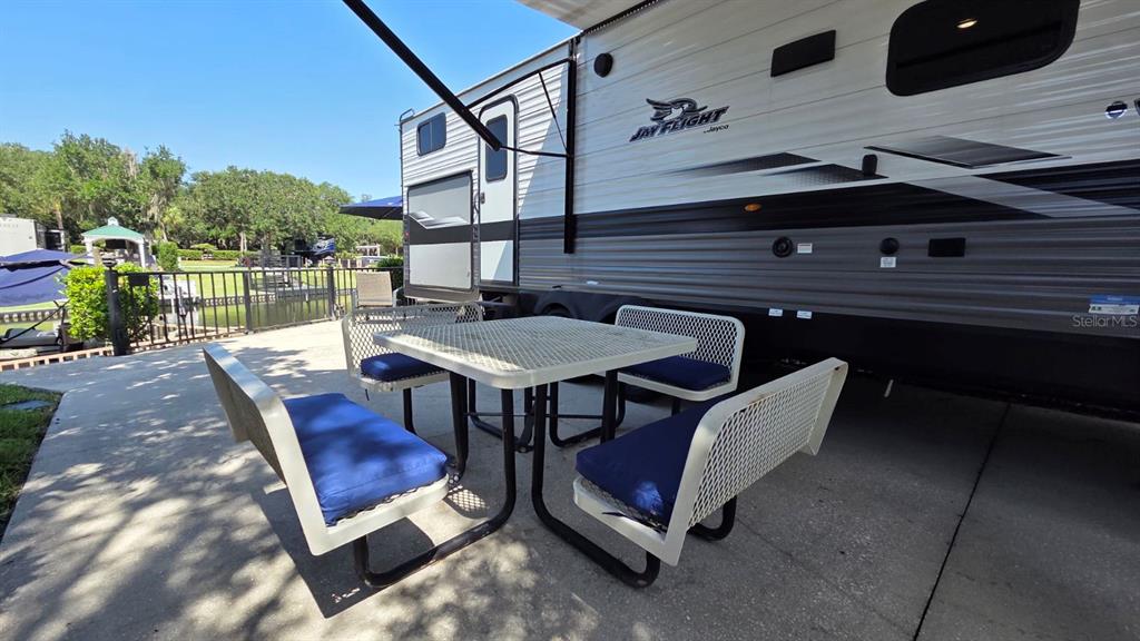A patio features a white metal picnic table with blue cushions beside a parked RV — 579 WATERWAY DRIVE, RIVER RANCH, FL