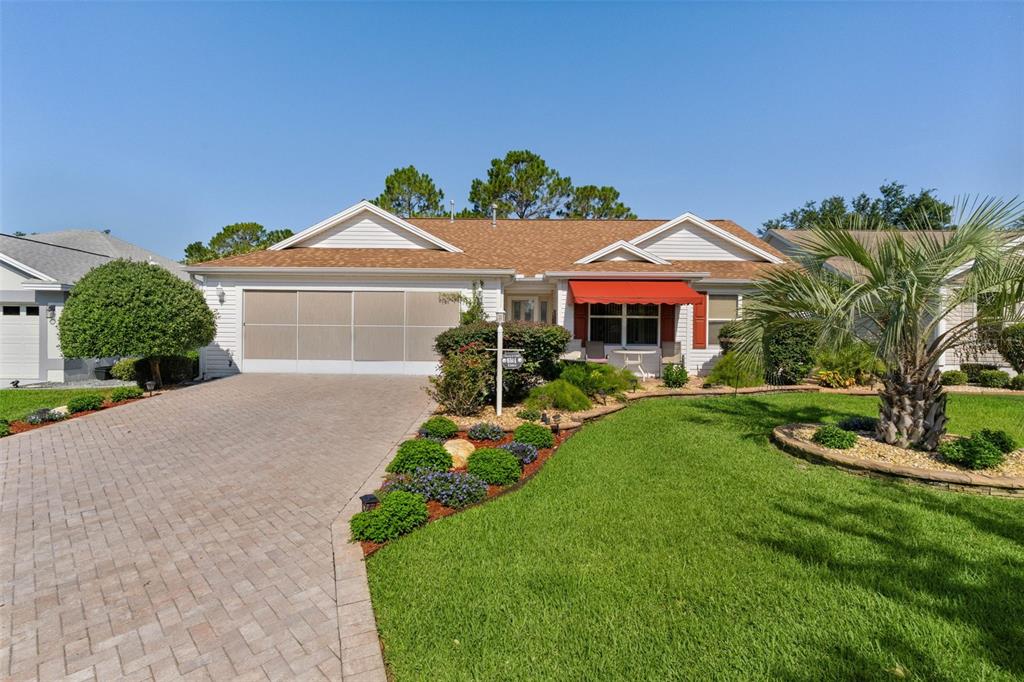 A single-story house with a paved driveway, a red awning, and a landscaped front yard — 16846 SE 80TH BELLAVISTA CIRCLE, THE VILLAGES, FL
