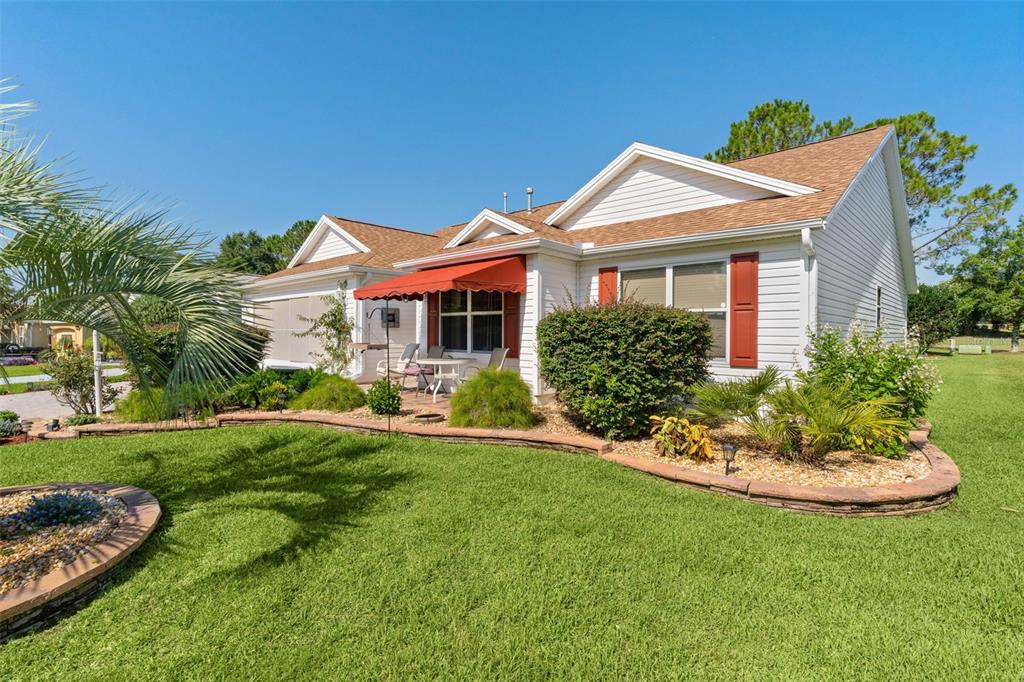 A white house with a red awning, a landscaped garden, and a green lawn — 16846 SE 80TH BELLAVISTA CIRCLE, THE VILLAGES, FL