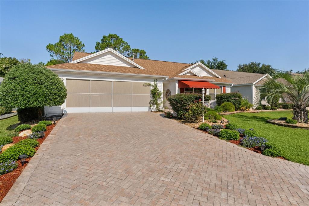 A single-story house with a paved driveway, a garage screen, and a red window awning — 16846 SE 80TH BELLAVISTA CIRCLE, THE VILLAGES, FL