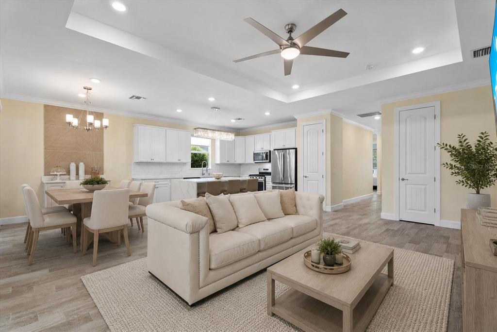 An open-concept living room and kitchen featuring a cream sofa, dining area, and white cabinetry — 12315 BLUE HILL TRAIL, BRADENTON, FL
