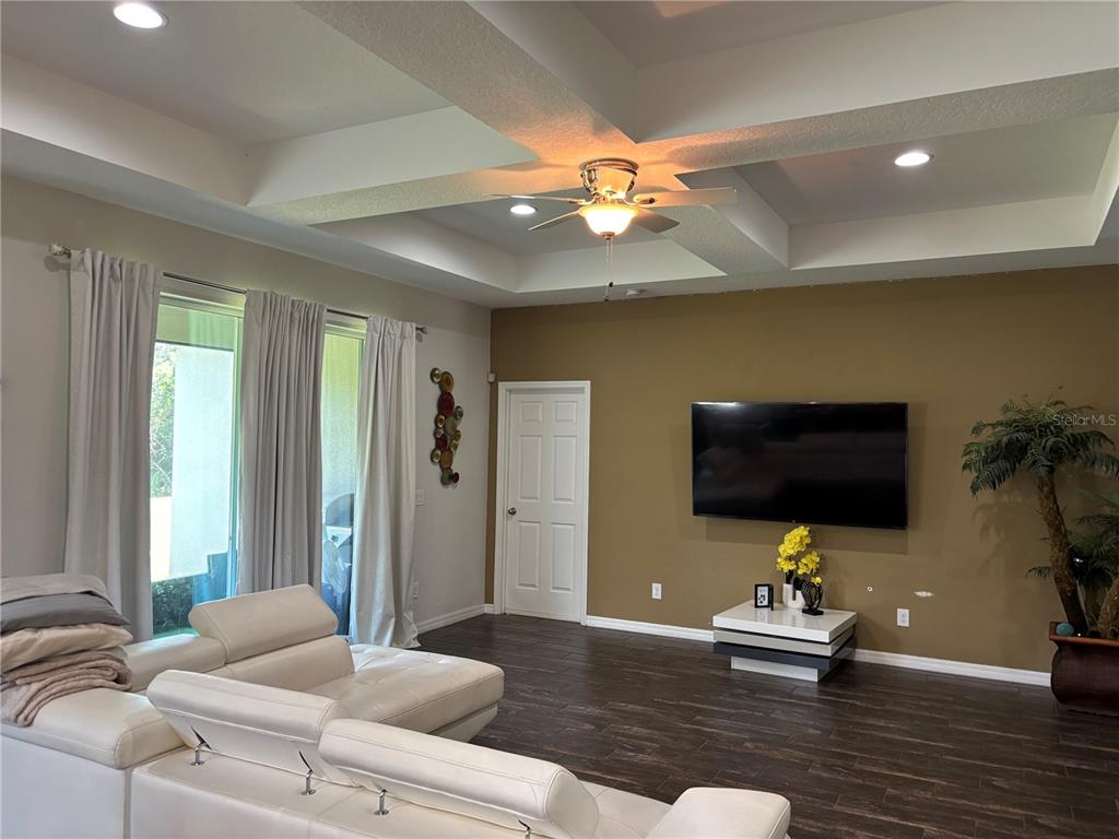 A living room features a white sectional sofa, a wall-mounted television, and a tray ceiling — 1727 BRASSIE COURT, KISSIMMEE, FL