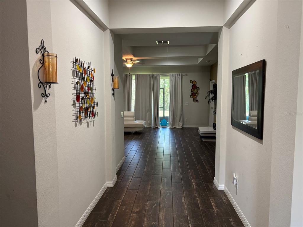 A hallway with dark wood-look tile flooring leads into a living area with white curtains — 1727 BRASSIE COURT, KISSIMMEE, FL