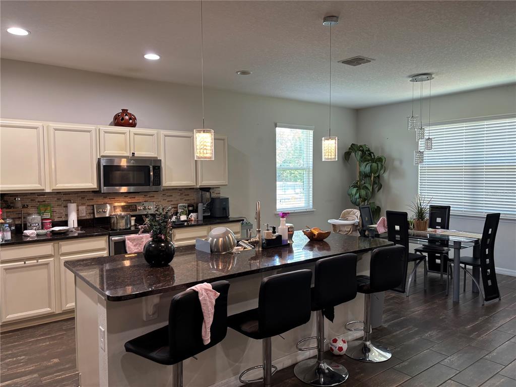 A kitchen features dark granite countertops, off-white cabinets, a center island, and a dining area — 1727 BRASSIE COURT, KISSIMMEE, FL