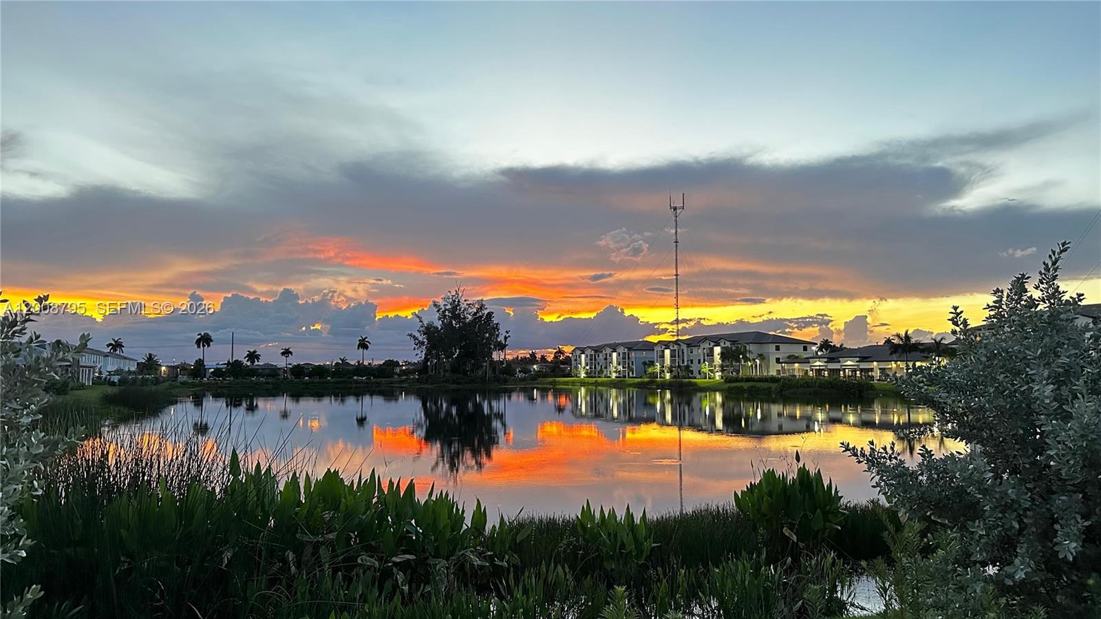 A pond reflects a sunset sky in front of apartment buildings and a communication tower — 20478 NW 4th Ct, Miami Gardens FL 33169, MIAMI GARDENS, FL