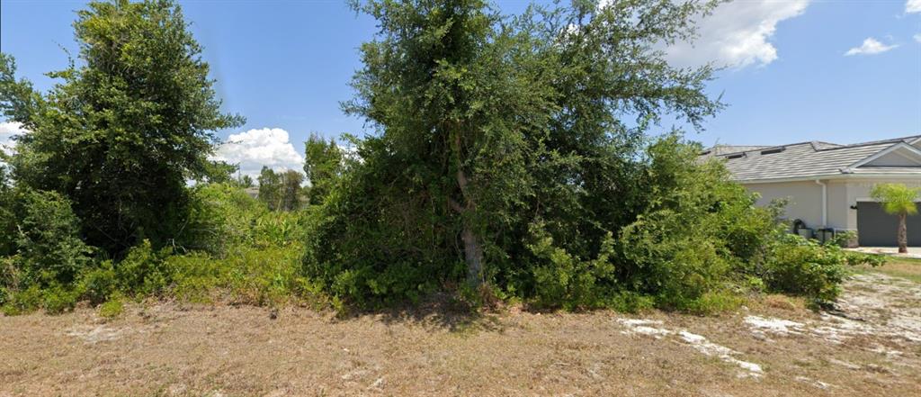 A vacant, overgrown residential lot sits next to a modern house with a gray roof — 9204 & 9196 RAVEL STREET, PORT CHARLOTTE, FL