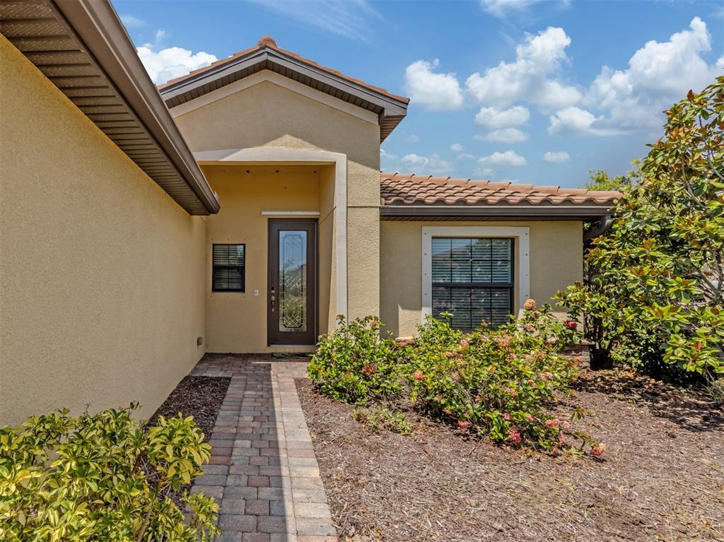 The exterior of a house features a tiled roof, stucco walls, and a brick walkway — 12490 CINQUETERRE DRIVE, VENICE, FL
