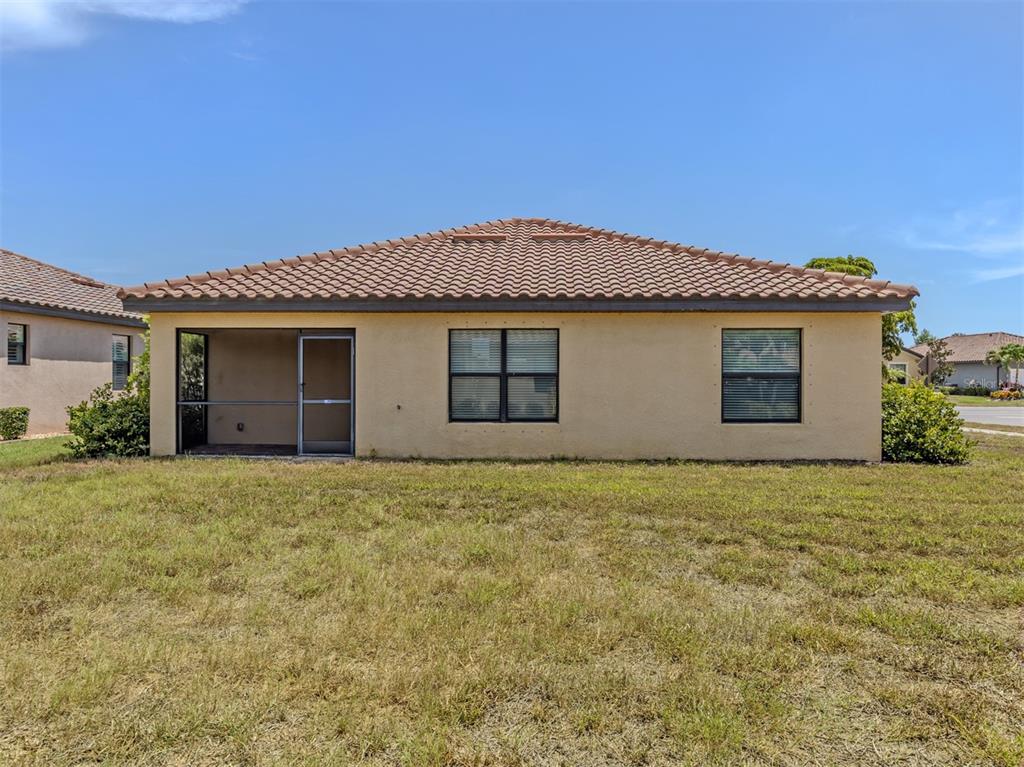The rear exterior of a tan stucco house features a screened lanai and two windows — 12490 CINQUETERRE DRIVE, VENICE, FL