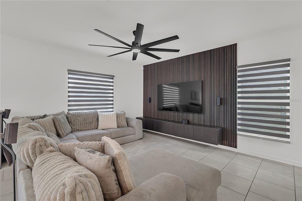 A living room features a large sectional sofa, a wall-mounted TV, and dark wood slat paneling — 1325 DIEGO TERRACE, WINTER HAVEN, FL