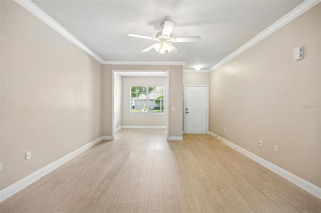 An empty living room features light wood-look flooring, beige walls, a ceiling fan, and a window — 405 SOUTHERN PECAN CIRCLE UNIT 108, WINTER GARDEN, FL