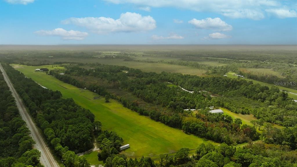 An aerial view shows a long grassy airstrip bordered by trees and a nearby road — 520 HIGHLANDER DRIVE Lot 5, OAK HILL, FL