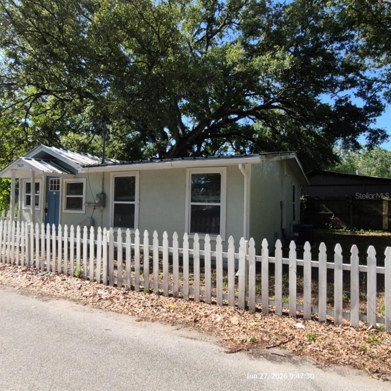 A light-colored single-story house with a metal roof stands behind a white picket fence — 7409 RHODE ISLAND DRIVE, TAMPA, FL
