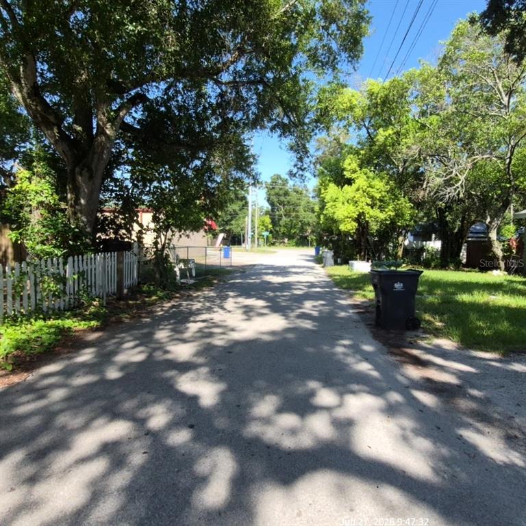 A paved alleyway lined with trees, a white picket fence, and a trash bin — 7409 RHODE ISLAND DRIVE, TAMPA, FL