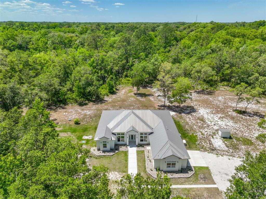 An aerial view shows a single-story house with a metal roof surrounded by dense forest — 1370 BUCKLES ROAD, PIERSON, FL