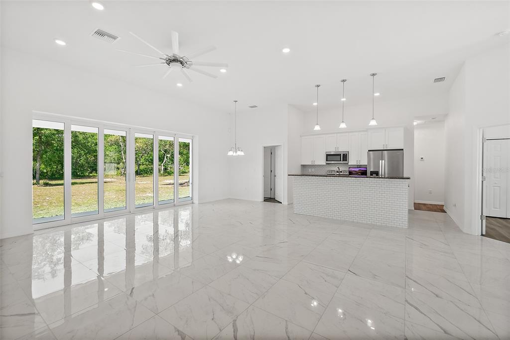 A bright, open-concept kitchen and living area features white cabinetry, marble-look tile floors, and sliding doors — 1370 BUCKLES ROAD, PIERSON, FL