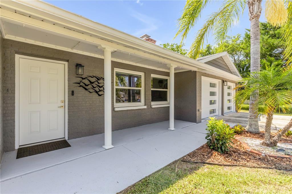 A gray brick house exterior features a white front door, porch columns, and a garage — 2716 KUMQUAT DRIVE, EDGEWATER, FL
