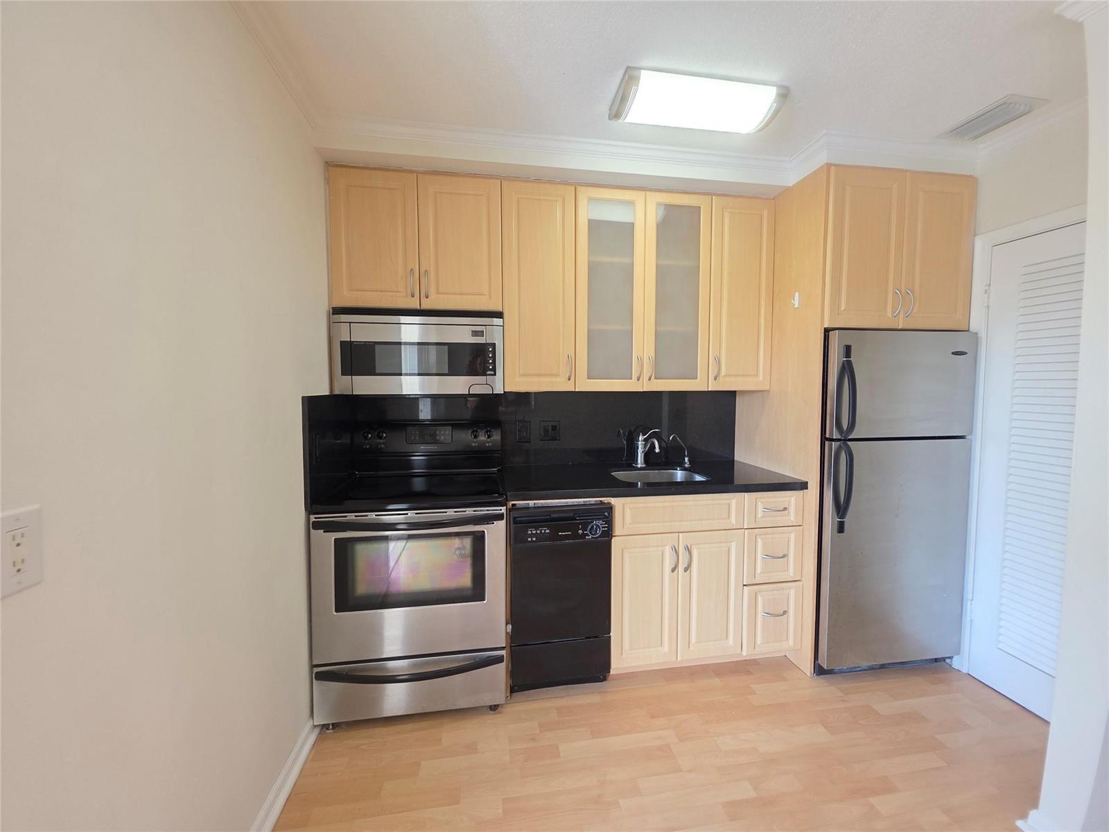A kitchen features light wood cabinets, stainless steel appliances, and a black countertop — 2131 NE 42nd Court # 208e, Lighthouse Point FL 33064, LIGHTHOUSE POINT, FL
