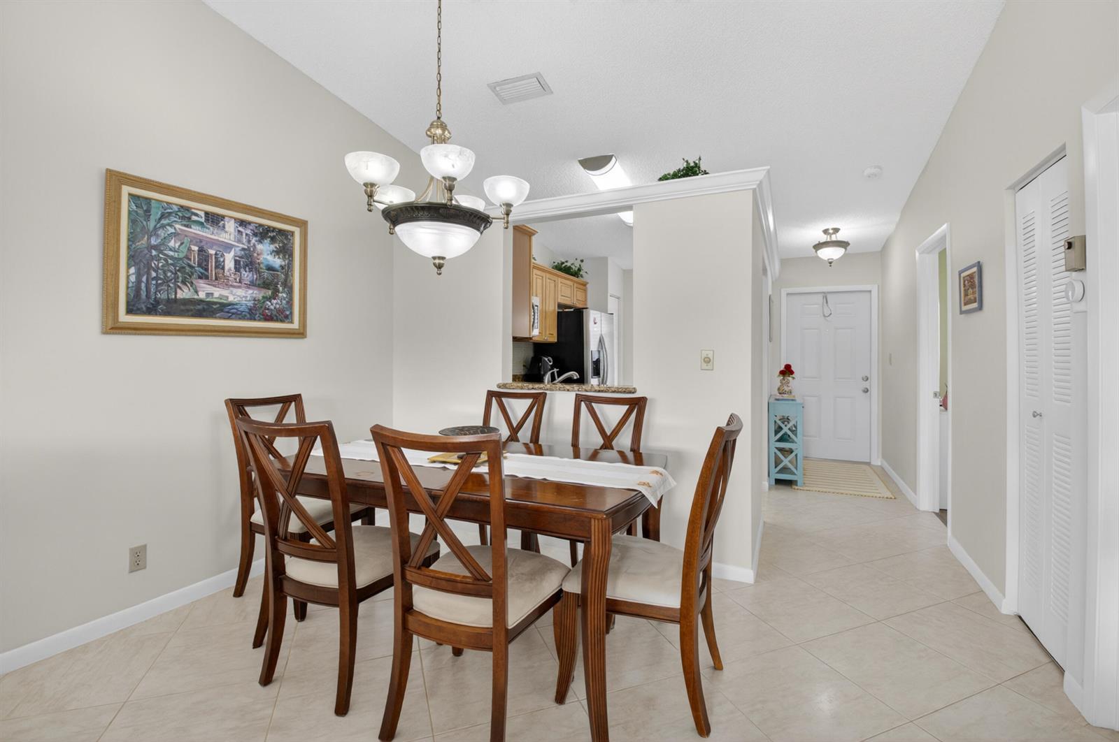 A dining area features a wooden table with six chairs under a chandelier near a kitchen — 18856 Argosy Drive # C, Boca Raton FL 33496, BOCA RATON, FL