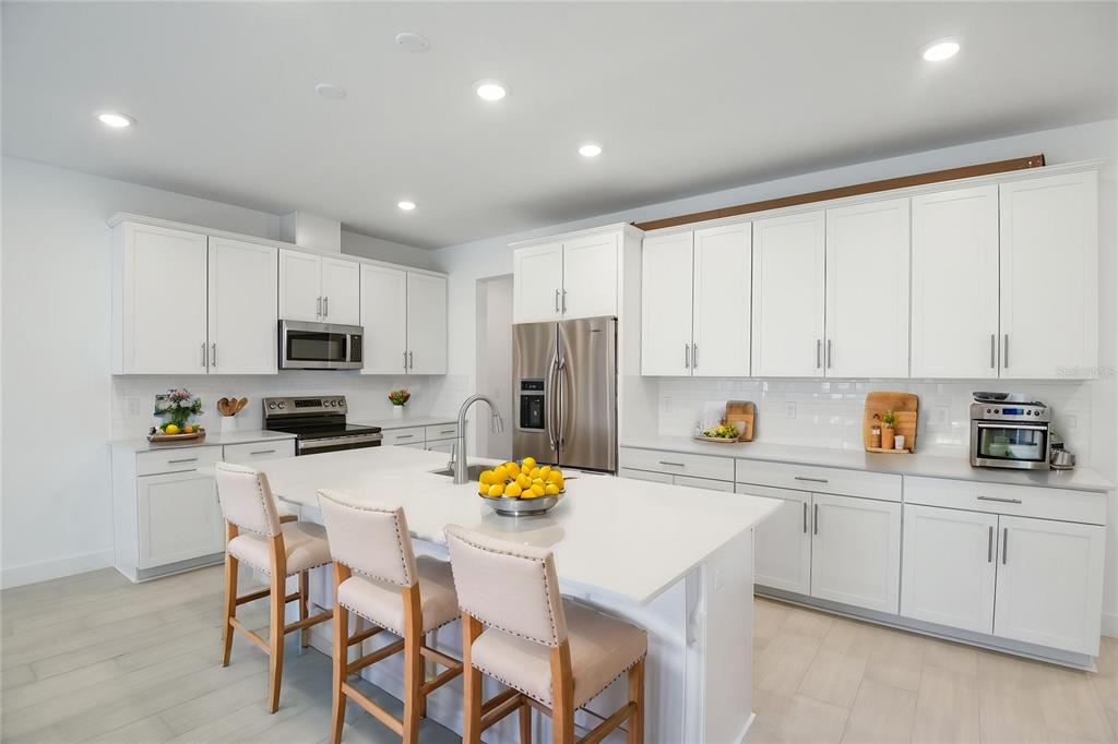 A modern kitchen features white cabinetry, a large central island with seating, and stainless appliances — 9093 PLAYERS DRIVE, WEEKI WACHEE, FL