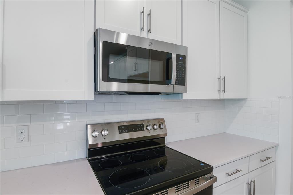 A kitchen features white cabinets, a stainless steel microwave, a glass-top stove, and subway tile — 9093 PLAYERS DRIVE, WEEKI WACHEE, FL